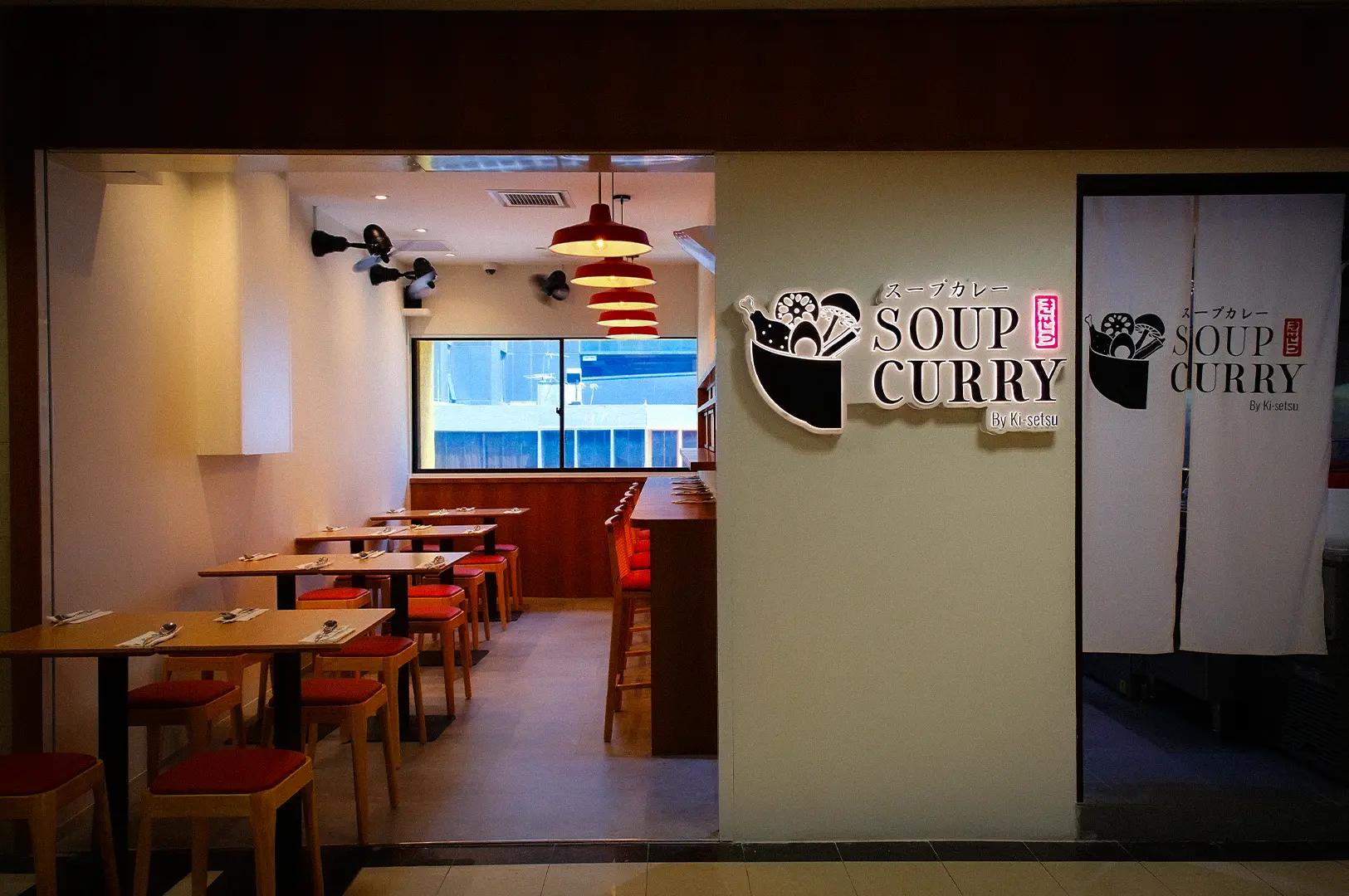 Soup Curry by Ki Setsu restaurant interior with Japanese-inspired decor, wooden tables, red stools, and illuminated signage.