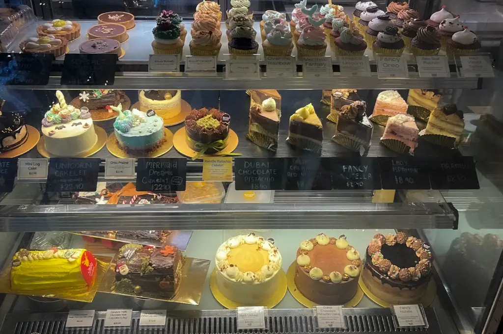 Glass display case filled with assorted gourmet cupcakes, cake slices, mini cakelets, and whole decorated cakes at Butter Studio in Bugis Junction, Singapore
