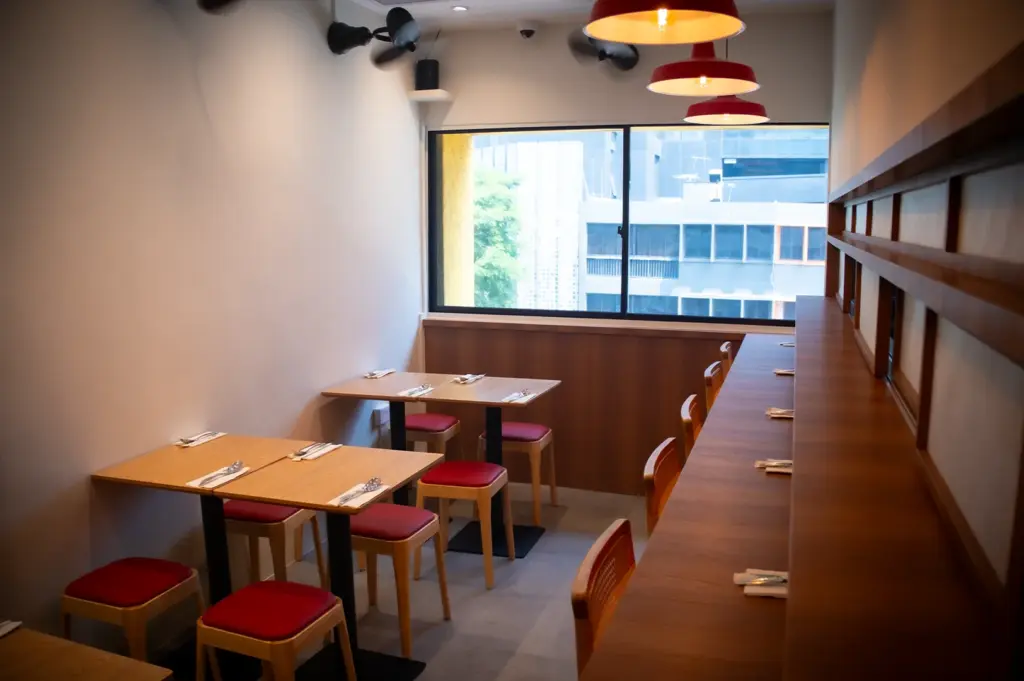 Soup Curry by Ki Setsu restaurant interior with wooden tables, red stools, counter seating, pendant lights, and large windows overlooking the city.