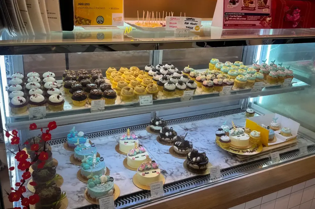Display cabinet featuring themed mini cakelets including unicorn and mermaid designs alongside rows of cupcakes at Butter Studio in Bugis Junction, Singapore
