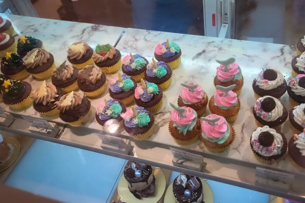 Top-down glass case view of assorted gourmet cupcakes with colorful buttercream frosting and themed toppers at Butter Studio in Bugis Junction, Singapore