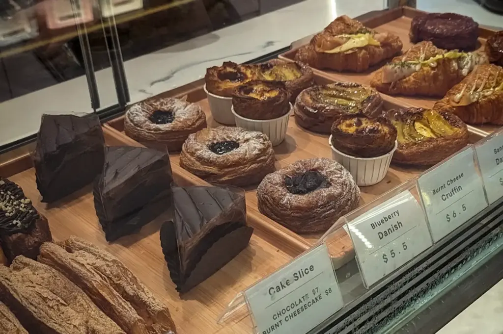 ASK Coffee Roastery Singapore pastry display featuring croissants, danishes, burnt cheesecake, chocolate cake, and assorted baked goods