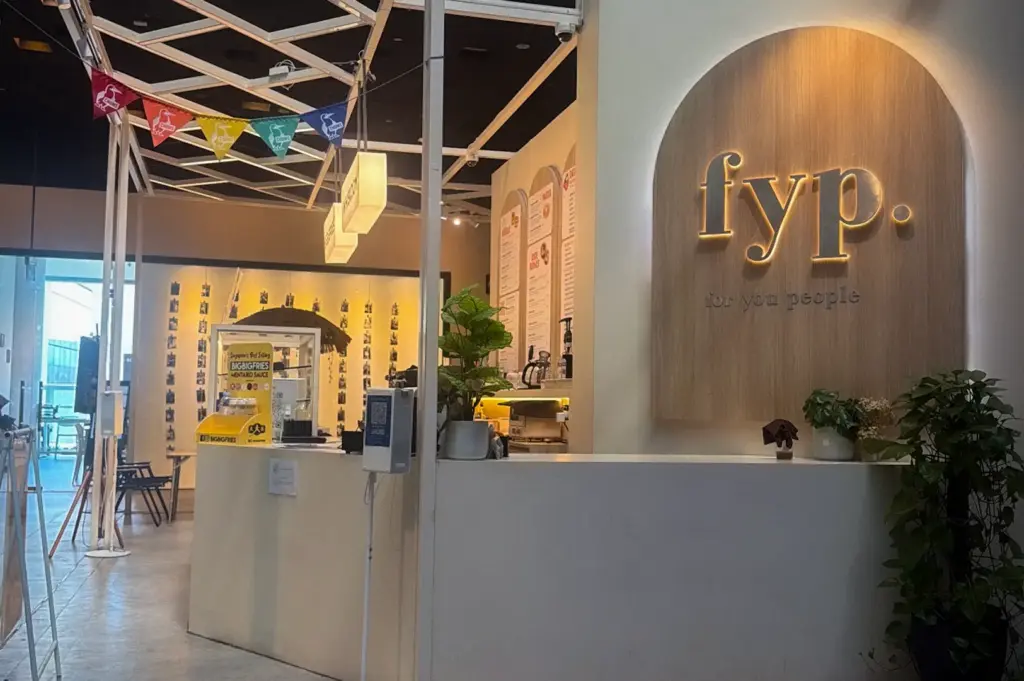 FYP Cafe Singapore interior with a minimalist cafe counter, illuminated FYP signage, seating area, and indoor plants.