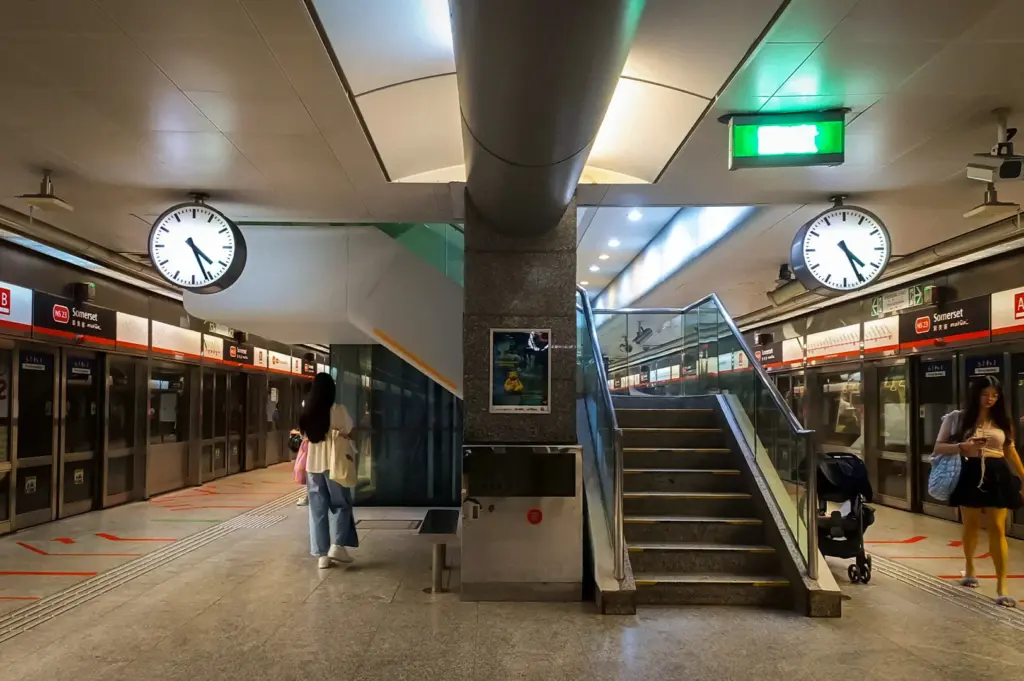 Somerset MRT Station in Singapore featuring platform screen doors, station clocks, escalators, emergency exit signage, and the North South Line platform interior.
