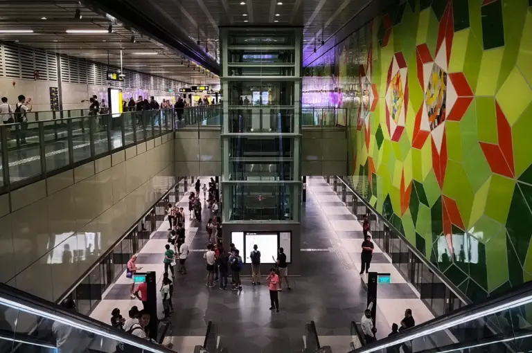 Underground platform view of Woodlands South MRT station along Singapore's Thomson-East Coast Line, featuring passenger platforms, an elevator shaft, and a colorful geometric wall art mural