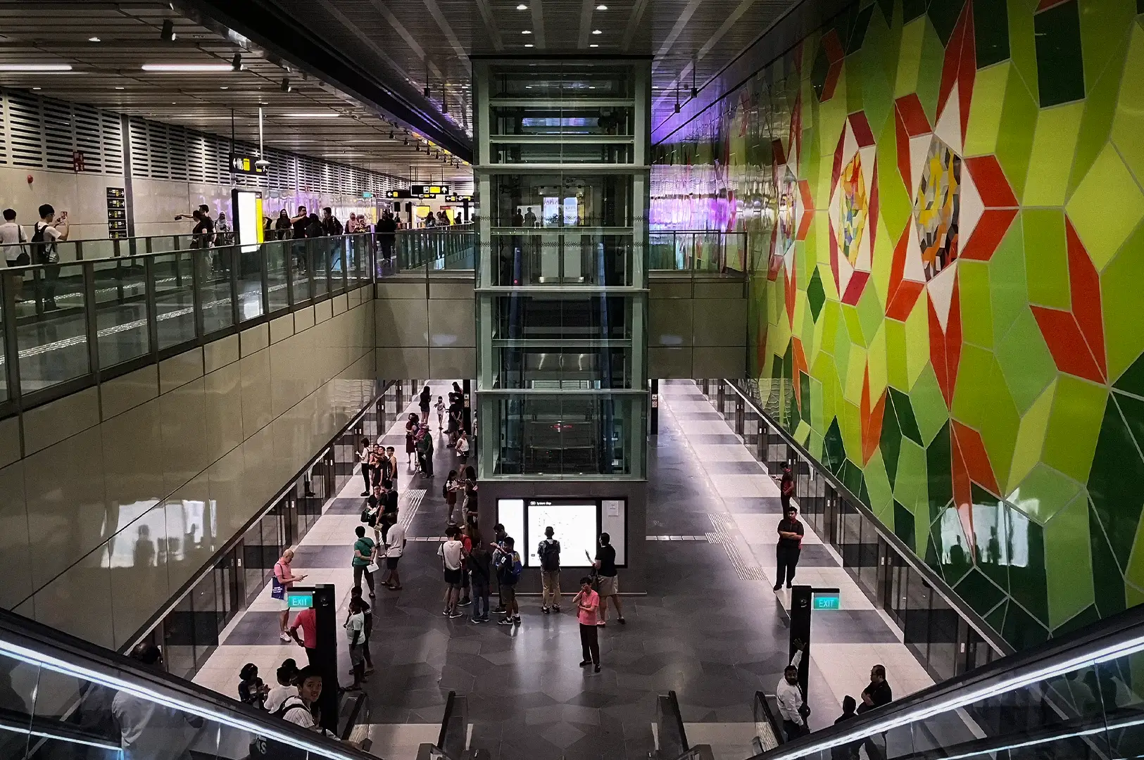 Underground platform view of Woodlands South MRT station along Singapore's Thomson-East Coast Line, featuring passenger platforms, an elevator shaft, and a colorful geometric wall art mural