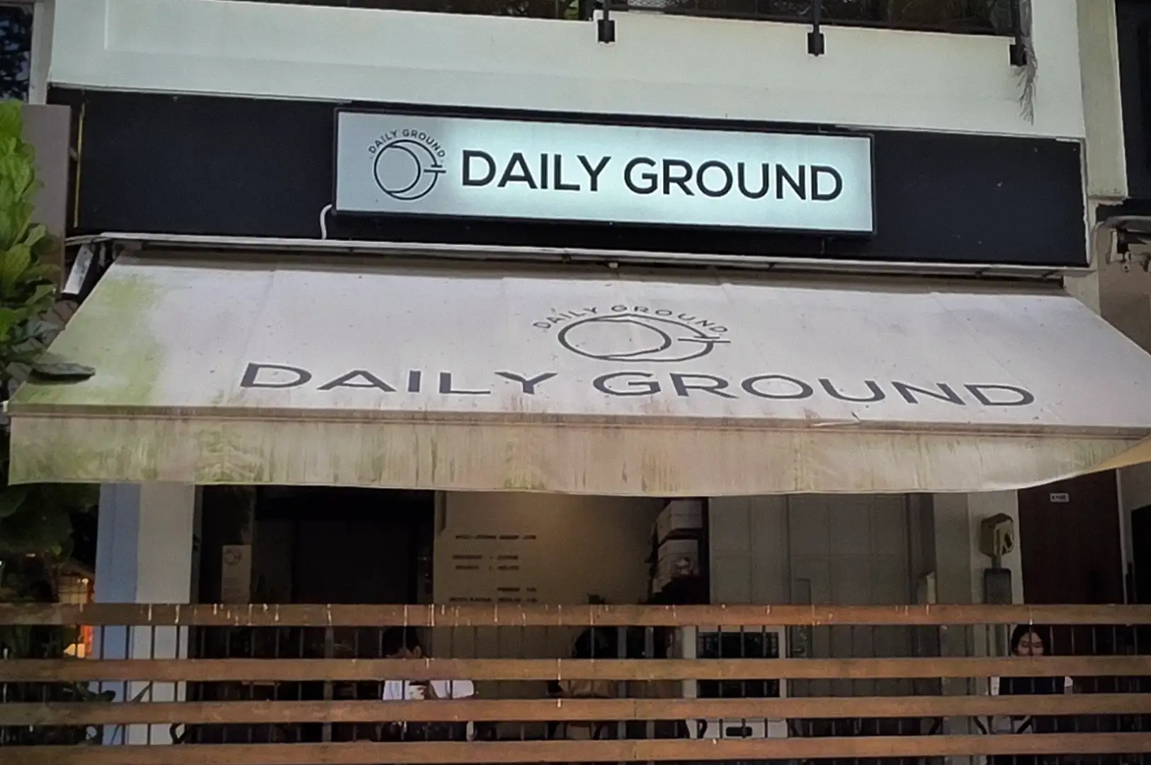 Exterior storefront view of Daily Ground cafe along Bukit Timah Road featuring a modern white facade, black sign, and sheltered outdoor seating area
