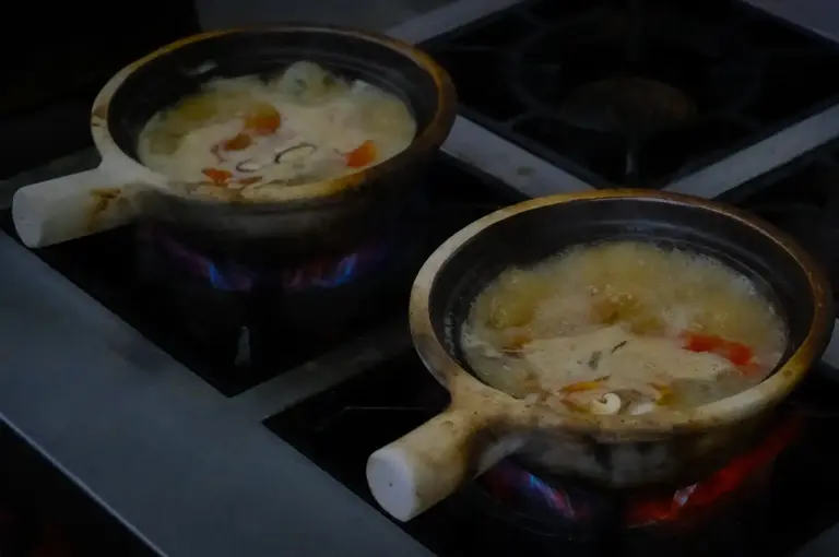 Claypots of fish soup boiling over active gas flames on a kitchen stove at Hup Lok near Tiong Bahru