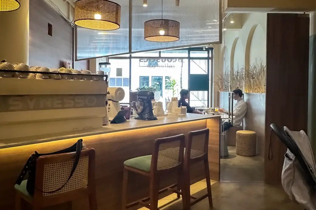 Cozy interior view of the espresso bar counter with wooden bar stools, woven pendant lights, and customers seated inside Acoustics Coffee Bar in Singapore