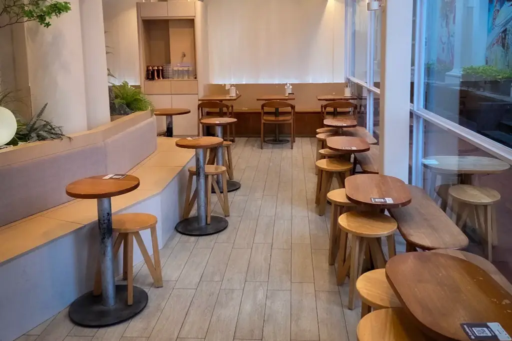 Minimalist dining interior of Glasshouse cafe at CHIJMES featuring light wooden tables, stools, and floor-to-ceiling glass windows in Singapore