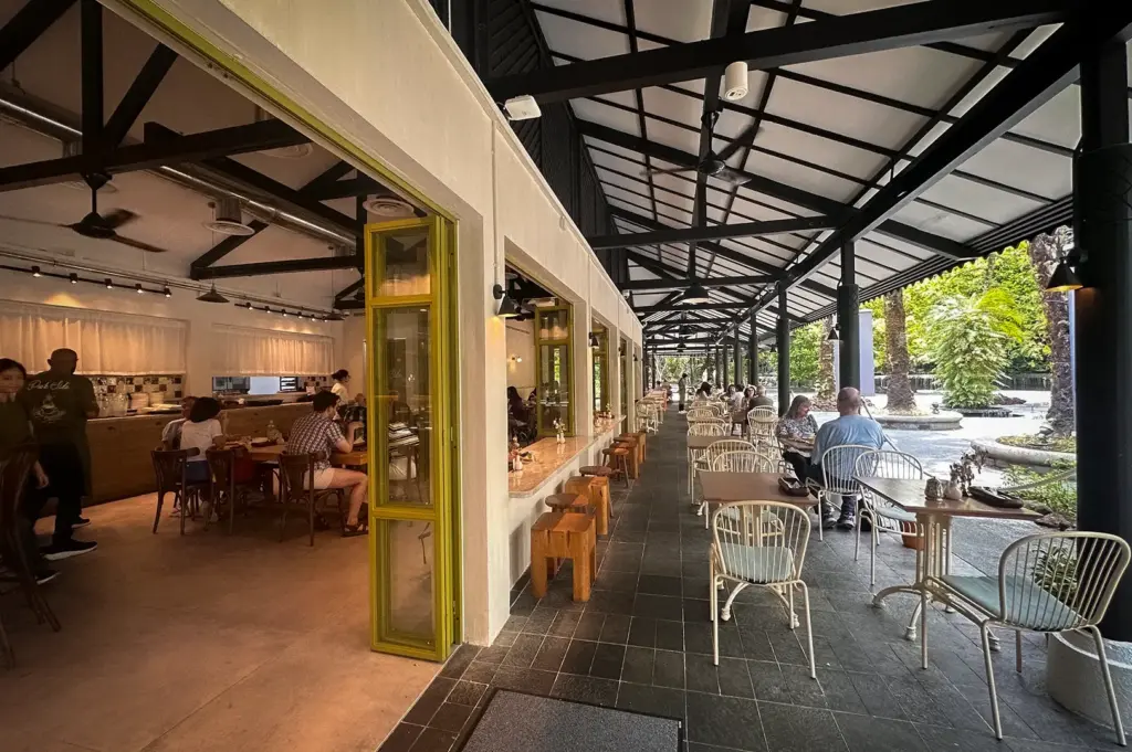 Outdoor terrace and indoor dining space at Park Side Cafe featuring metal truss roofing, patio tables and chairs, and patrons dining along the walkway