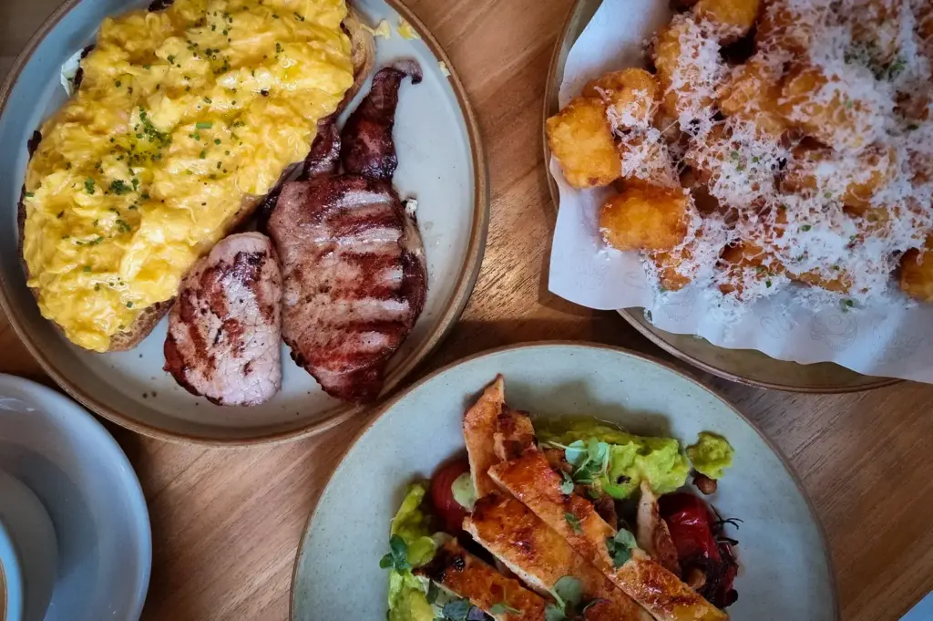 Café brunch spread featuring creamy scrambled eggs on toast with bacon, grilled chicken avocado salad, and parmesan tater tots at Glasshouse in CHIJMES, Singapore