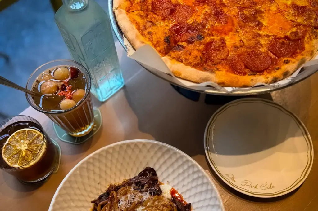 Spread of pepperoni pizza, pasta and specialty drinks on a wooden table at Park Side Cafe