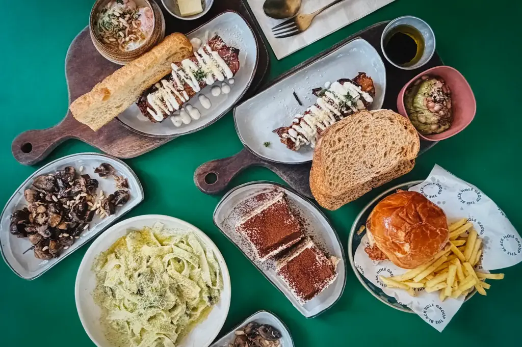 An overhead view of a varied brunch spread at Small Batch cafe in Singapore, featuring pasta, burgers with fries, open-faced sandwiches, mushroom dishes, and desserts arranged on a bright surface.