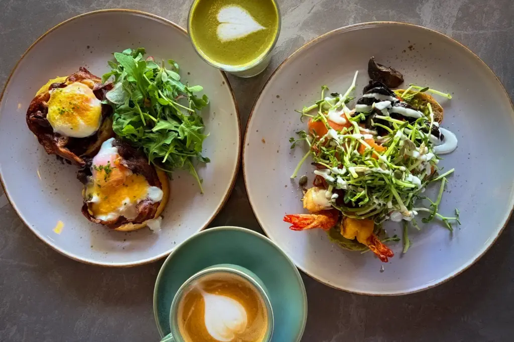Wildseed Café brunch spread featuring gourmet egg dishes, a seafood salad toast, a hot latte with heart latte art, and a matcha green tea latte on a table
