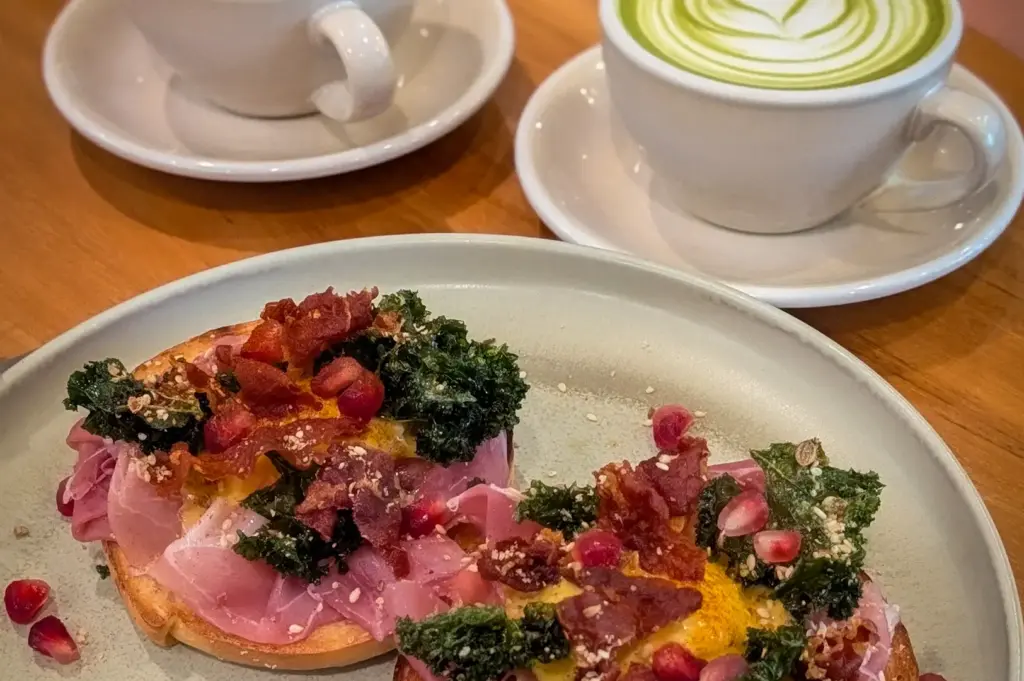 Prosciutto eggs benedict topped with crispy kale and pomegranate seeds served alongside caffe latte and matcha latte at Glasshouse in CHIJMES, Singapore