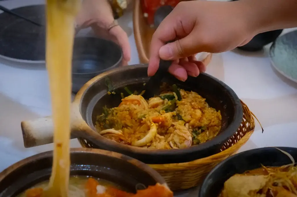 A close-up of a steaming claypot of seafood rice being served at the table at Hup Lok near Tiong Bahru, accompanied by bowls of claypot noodles and soup