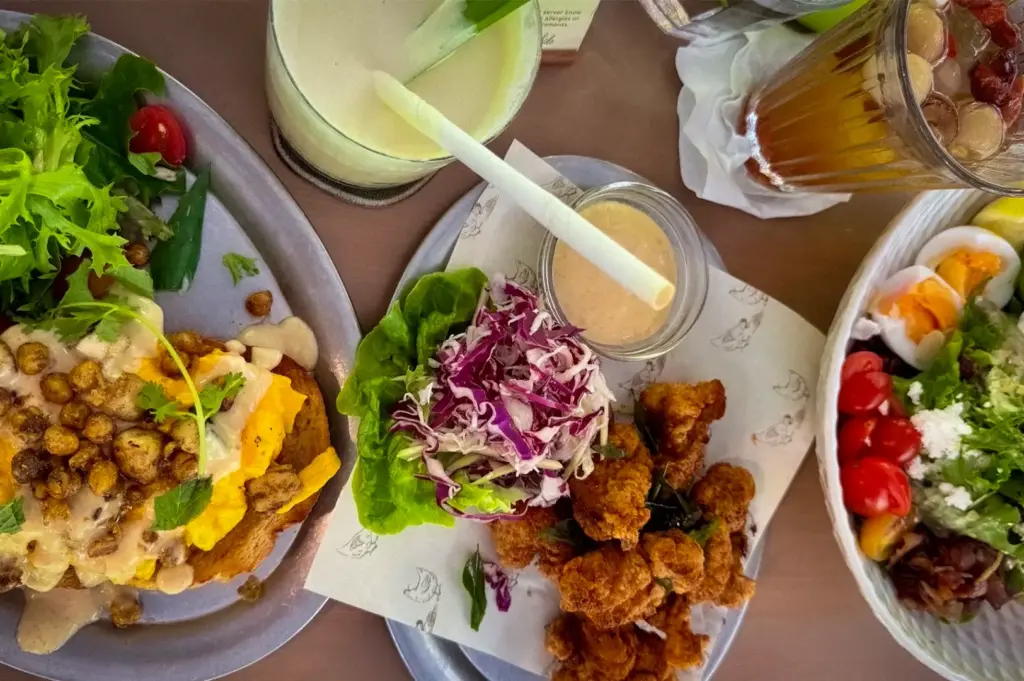 Hearty brunch spread at Park Side Cafe featuring a fresh salad, fried chicken with coleslaw, scrambled eggs on toast, and refreshing drinks on a table
