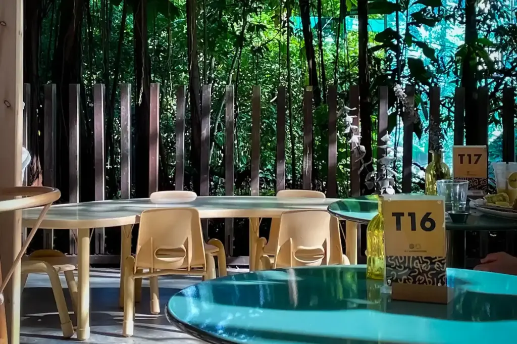 A table view inside Small Batch cafe in Singapore, featuring round tables with numbered table tents, overlooking a rustic fence and dense green foliage outside.