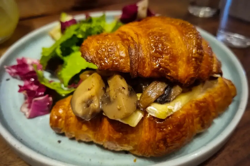 Golden flaky croissant sandwich filled with sautéed mushrooms and melted brie, served alongside a side salad at Acoustics Coffee Bar in Singapore