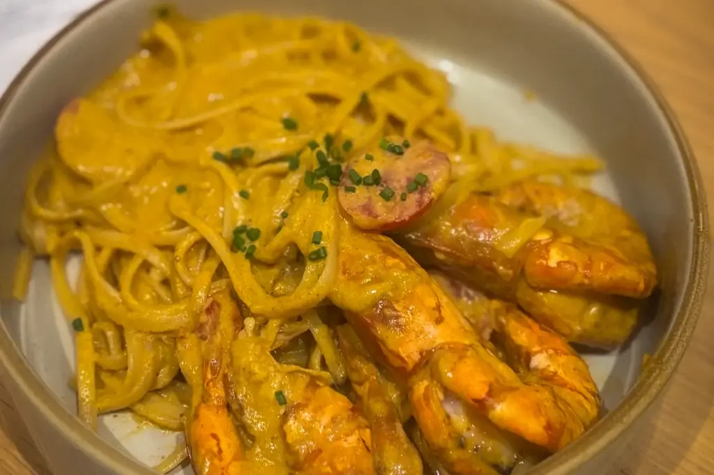 Wildseed Café serving of prawn pasta coated in a rich creamy sauce garnished with chopped chives in a shallow bowl