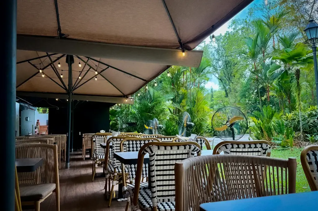 Wildseed Café outdoor patio dining area featuring shaded tables under large umbrellas looking out toward lush green trees and gardens