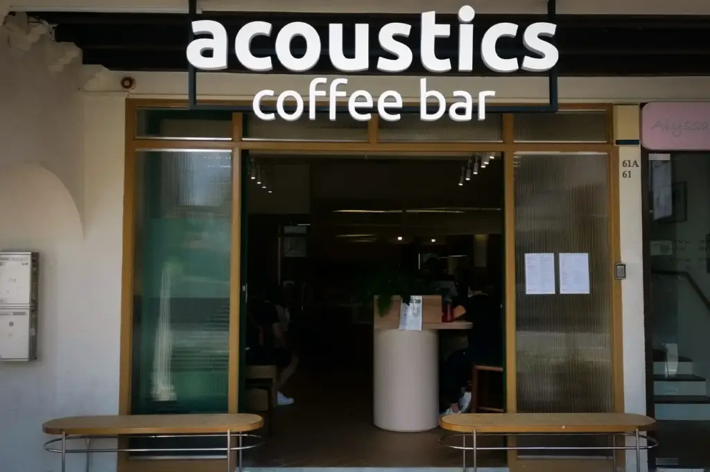 Daylight view of the bold white storefront signage and open wooden entryway of Acoustics Coffee Bar along Neil Road in Singapore